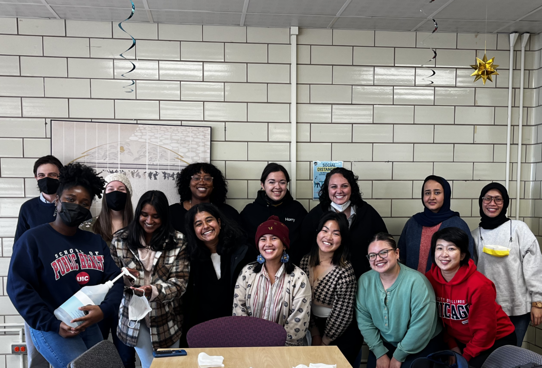 Photo of 14 MCH MPH students that is featured as the header in this newsletter, gathered around a table in front of subway tile wall, smiling at the camera