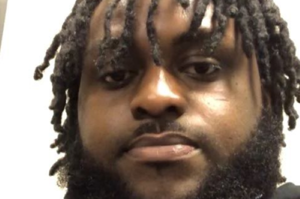 Man with thick beard and dreadlocks hanging down at eye and ear level looking directly at camera in close shot