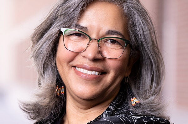 Woman with salt and pepper shoulder length hair, tan skin, and glasses smiling at camera