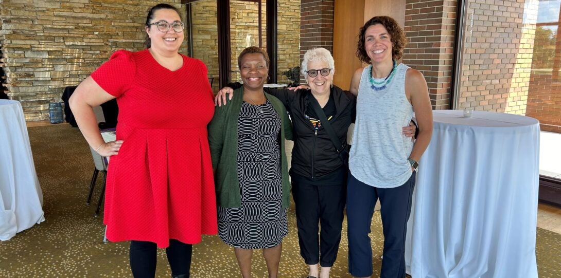 four women with arms around each other standing and smiling at camera